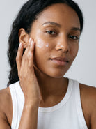 SILNT Plumping Serum applied to a model's cheek with her fingertips, white tank top, light grey background