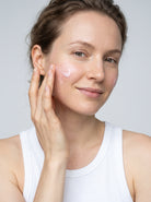 Smiling woman in a white tank top smoothing SILNT Exosome Serum onto her face