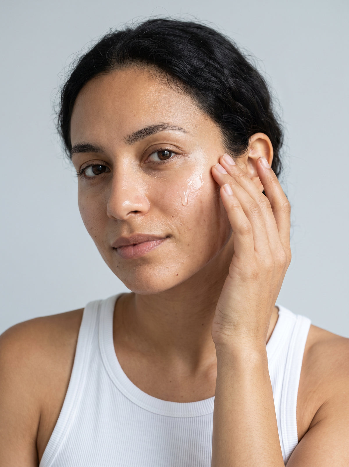 Woman in a white tank top smoothing SILNT Prebiotic Serum onto both cheeks