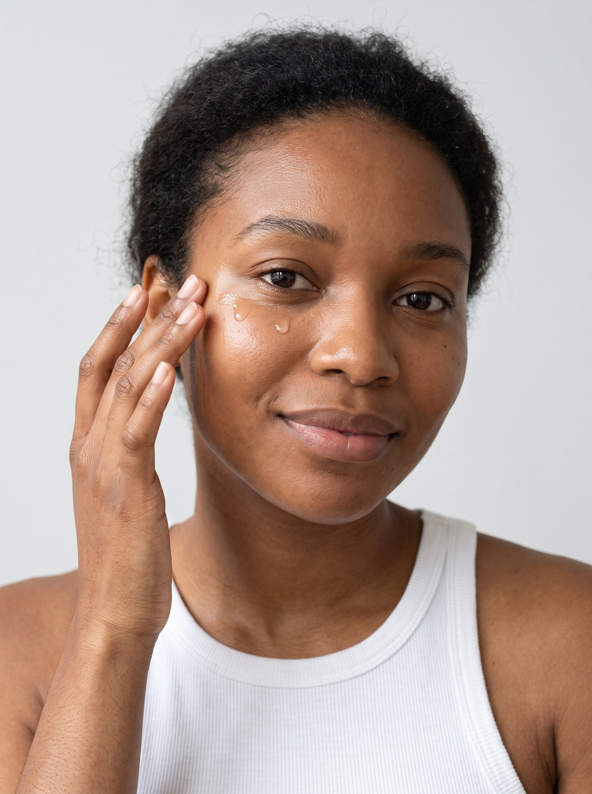 Woman in a white tank top applying SILNT Caffeine Booster to her under-eye area