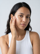 SILNT Exfoliating Concentrate pressed into a model's cheek with her fingertips, white tank top, light grey background