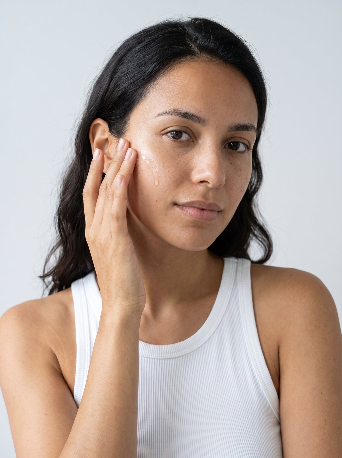 SILNT Exfoliating Concentrate pressed into a model's cheek with her fingertips, white tank top, light grey background