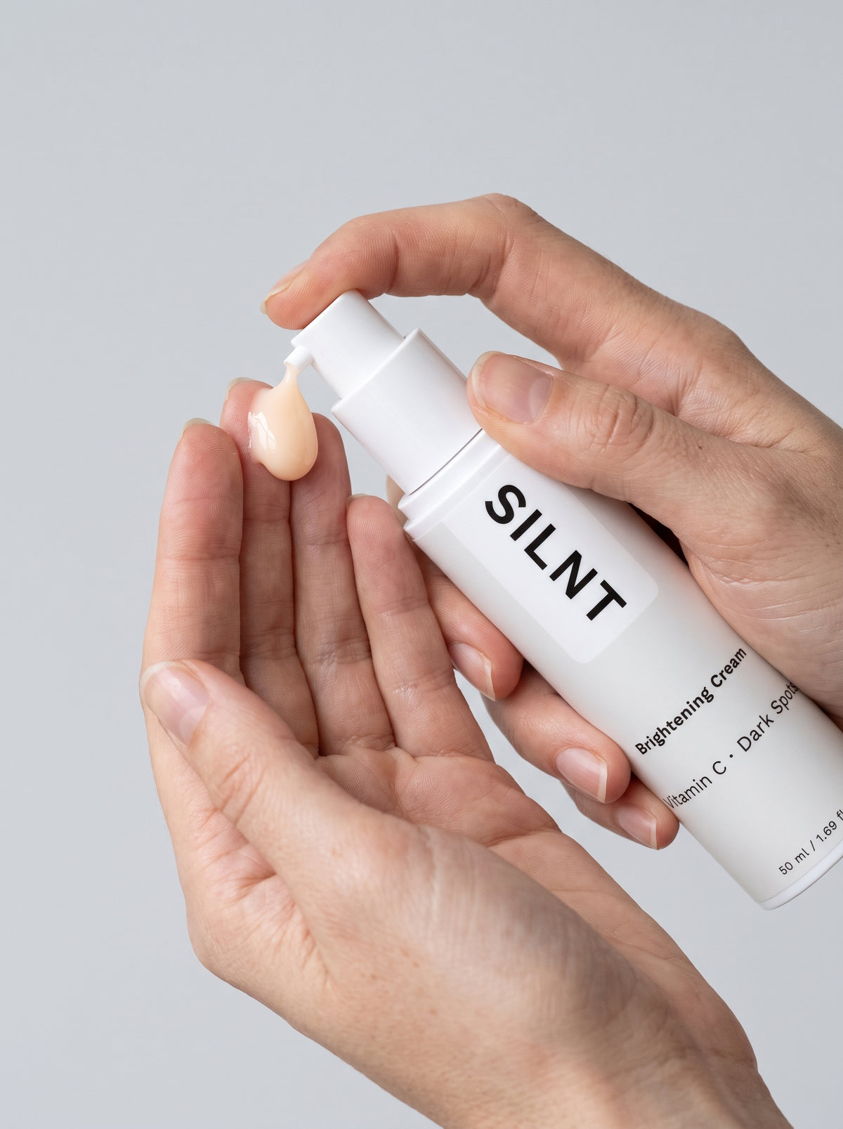 Hand holding the SILNT Brightening Cream pump bottle upright