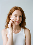 Red-haired woman in a white tank top applying SILNT Glycolic Toner with a cotton pad
