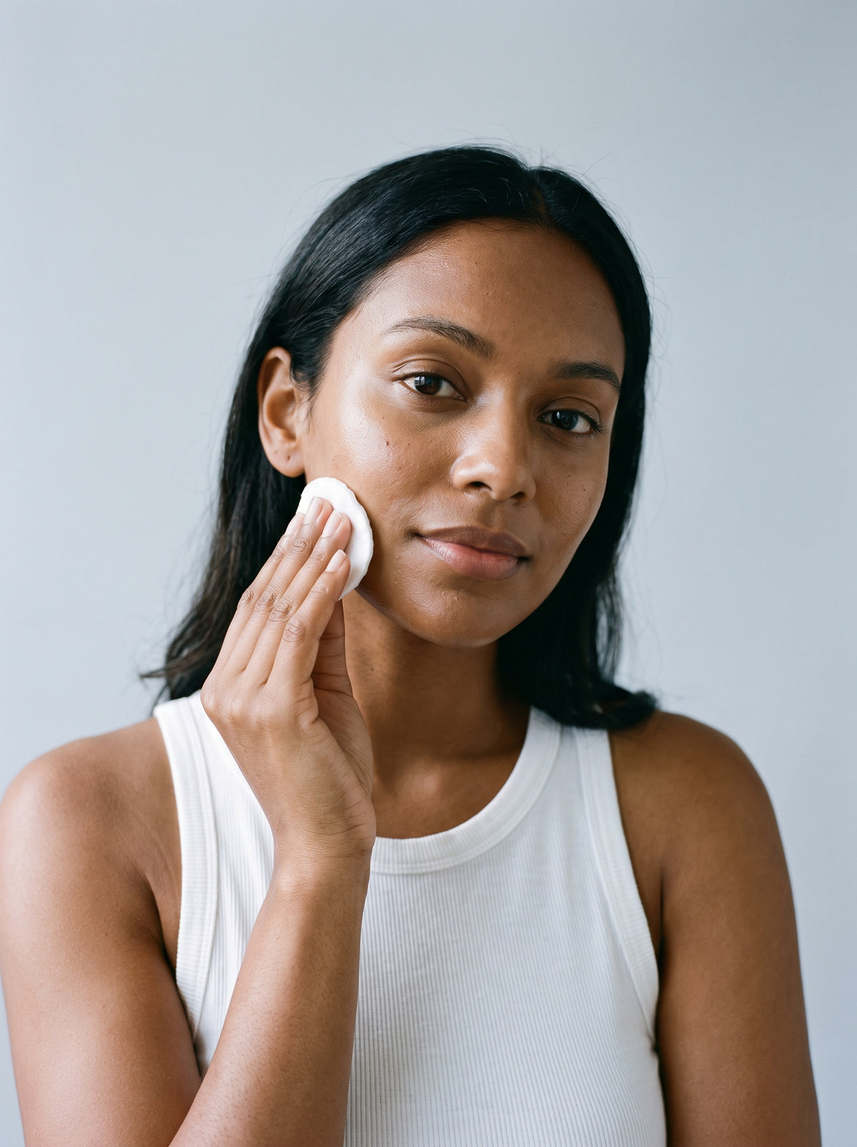 SILNT Makeup Remover swept over a model's cheek with a cotton pad, white tank top, light grey background