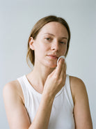 SILNT Makeup Remover swept over a model's cheek with a cotton pad, white tank top, light grey background