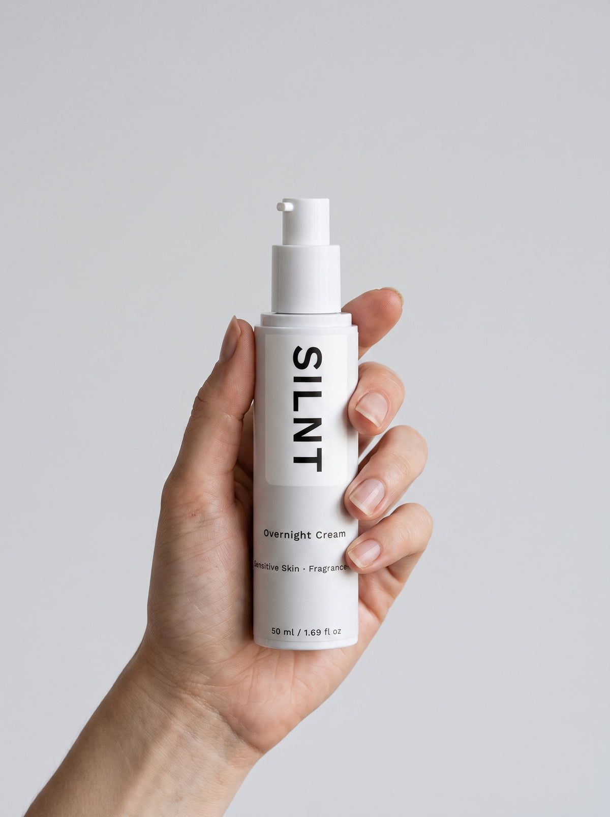A hand holding SILNT Overnight Cream against a light grey background