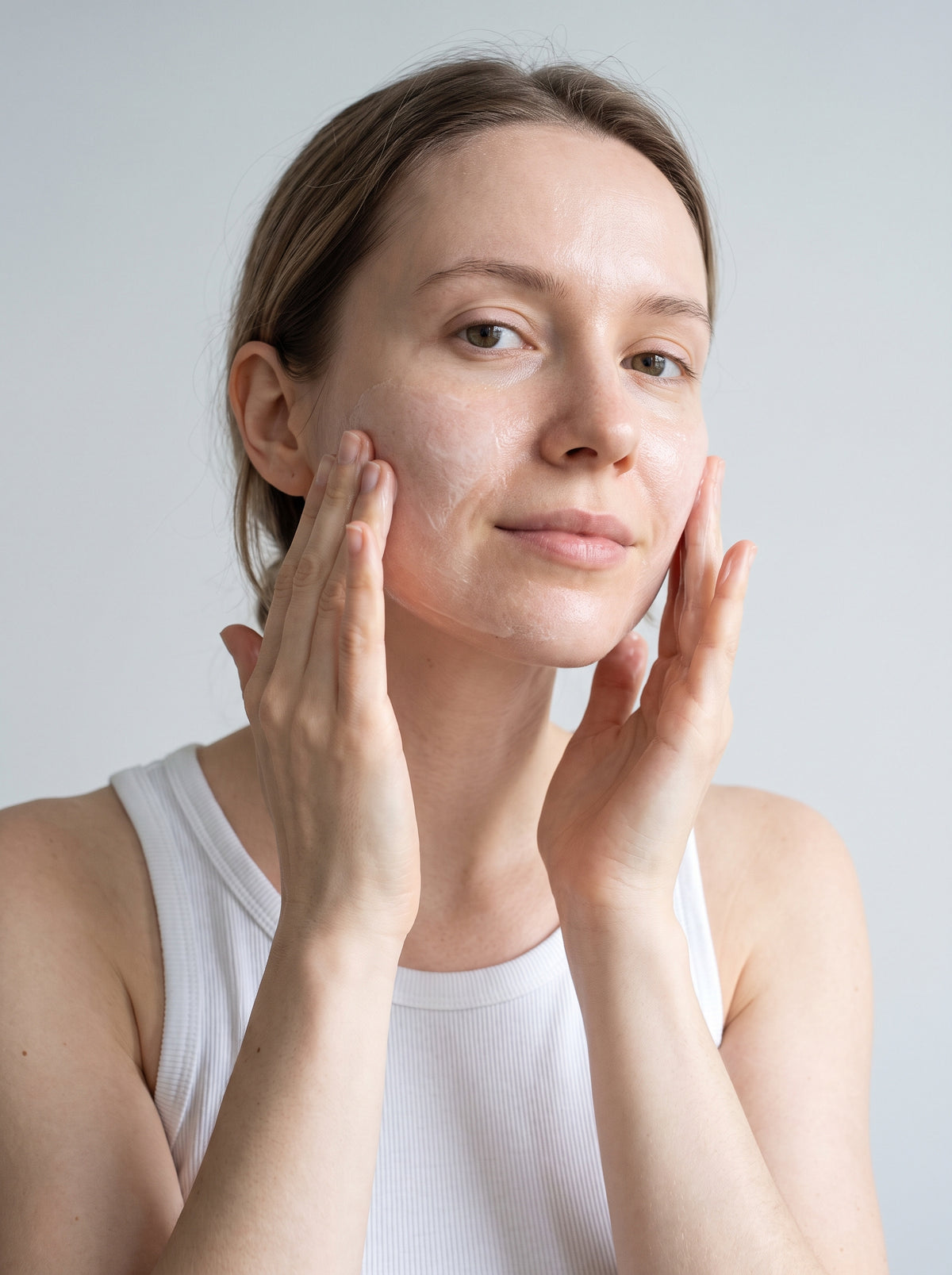 SILNT Cleansing Milk massaged over a model's cheeks with both hands, white tank top, light grey background