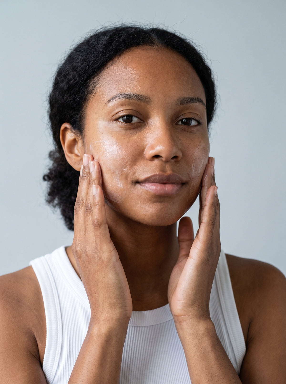 SILNT Cleansing Milk massaged over a model's cheeks with both hands, white tank top, light grey background