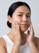 SILNT Clarifying Cleanser massaged over a model's cheeks with both hands, white tank top, light grey background