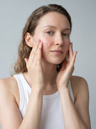 SILNT Radiance Cleanser massaged over a model's cheeks with both hands, white tank top, light grey background