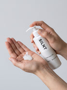 SILNT Cleansing Milk white lotion dispensed into an open palm from the pump bottle, light grey background