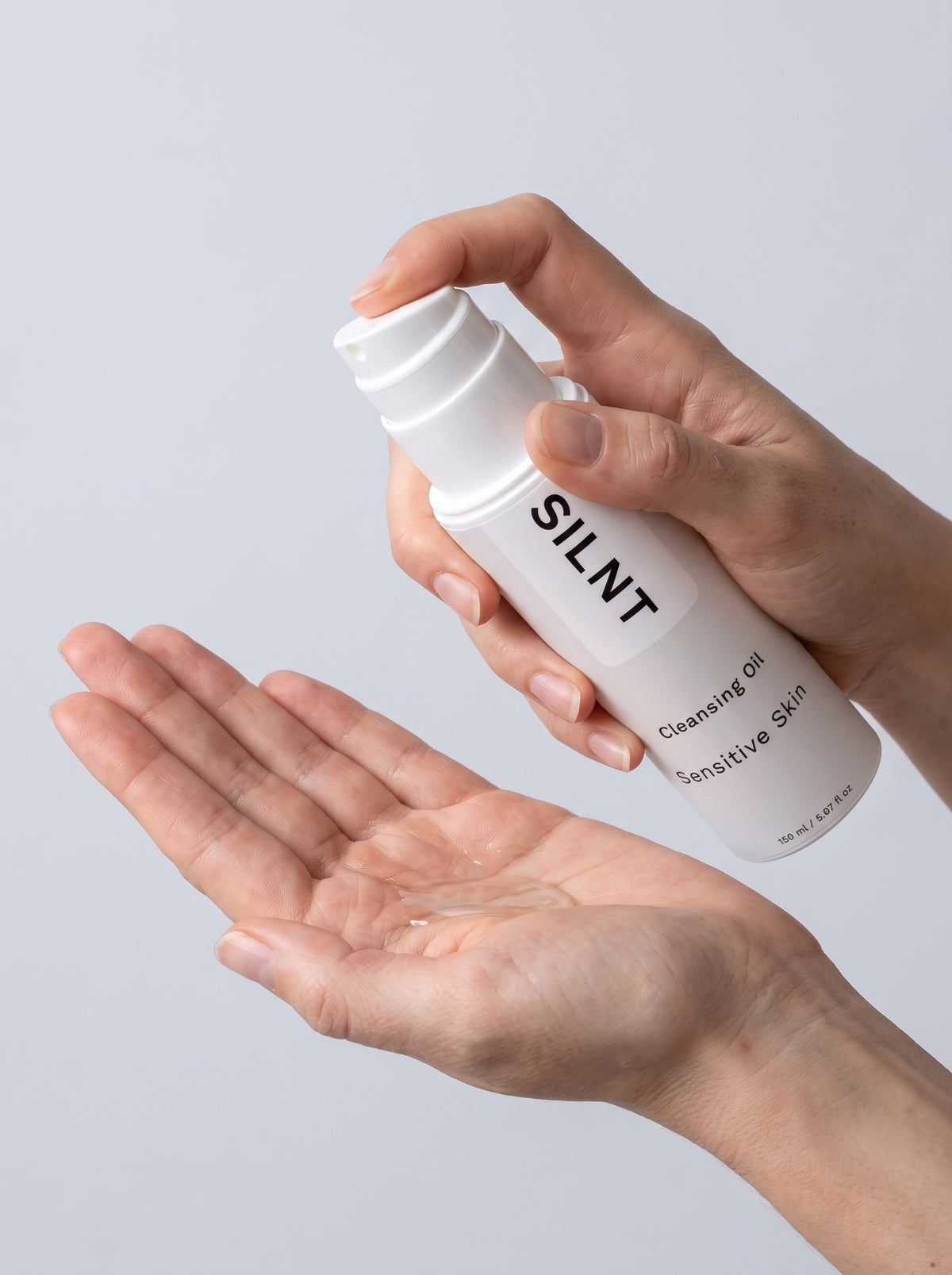 SILNT Cleansing Oil clear oil dispensed into an open palm from the pump bottle, light grey background