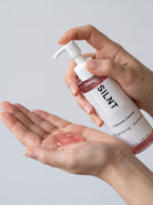 SILNT Radiance Cleanser pink gel dispensed into an open palm from the pump bottle, light grey background