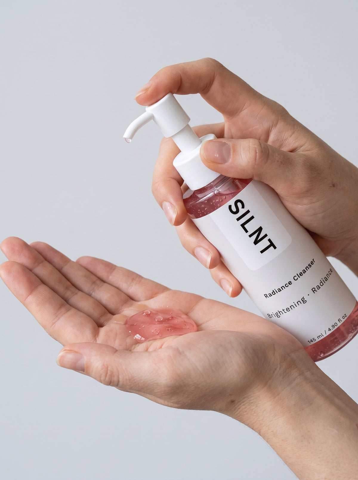 SILNT Radiance Cleanser pink gel dispensed into an open palm from the pump bottle, light grey background