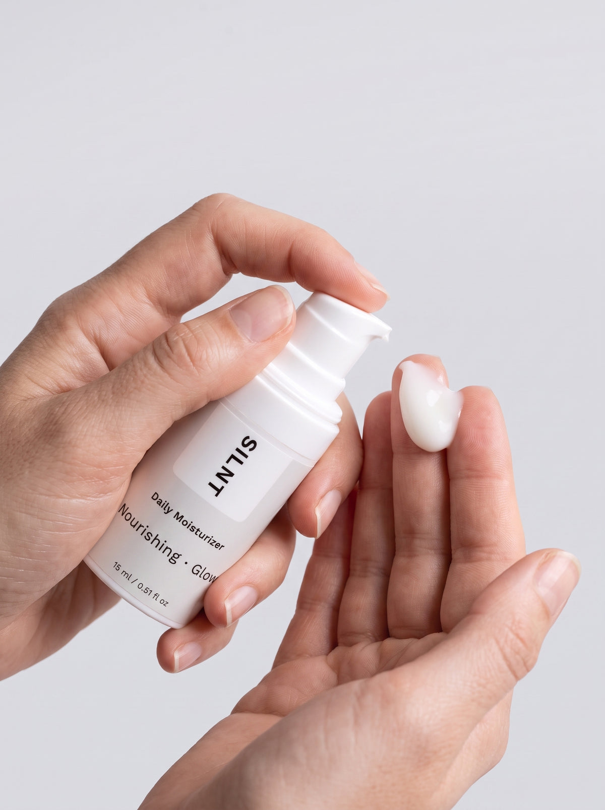 SILNT Daily Moisturizer travel size bottle dispensing white cream onto fingertips, light grey background