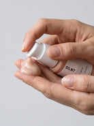 SILNT Peptide Serum bottle held in both hands with the pump facing forward, light grey background