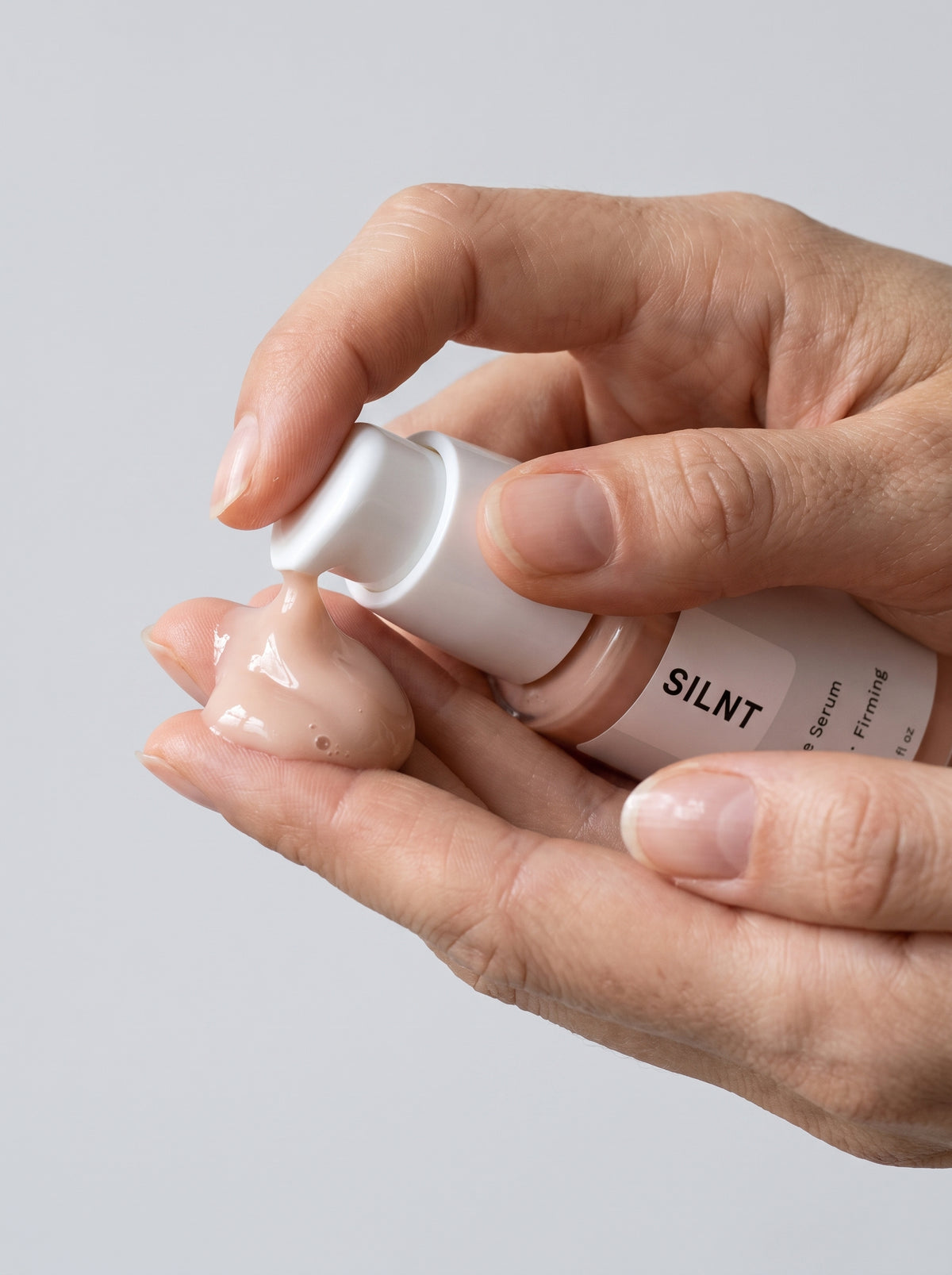 SILNT Peptide Serum bottle held in both hands with the pump facing forward, light grey background