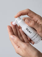 SILNT Retinol Alternative Cream bottle dispensing pale pink cream onto fingertips, light grey background