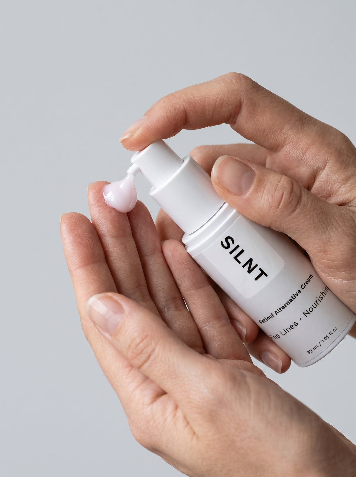 SILNT Retinol Alternative Cream bottle dispensing pale pink cream onto fingertips, light grey background