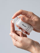 SILNT Eye Cream bottle dispensing white cream onto a fingertip, light grey background