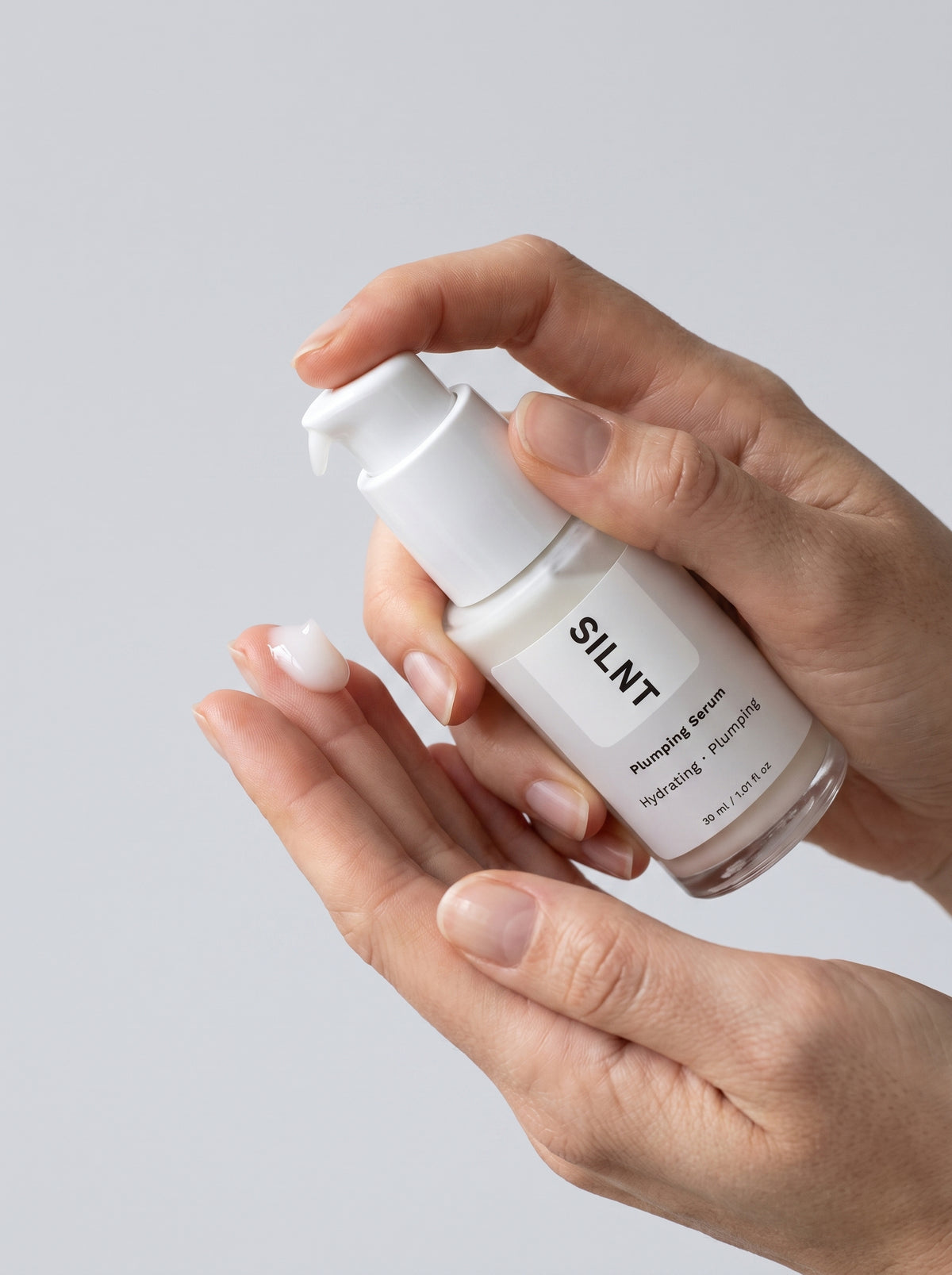 SILNT Plumping Serum bottle dispensing milky white serum onto fingertips, light grey background