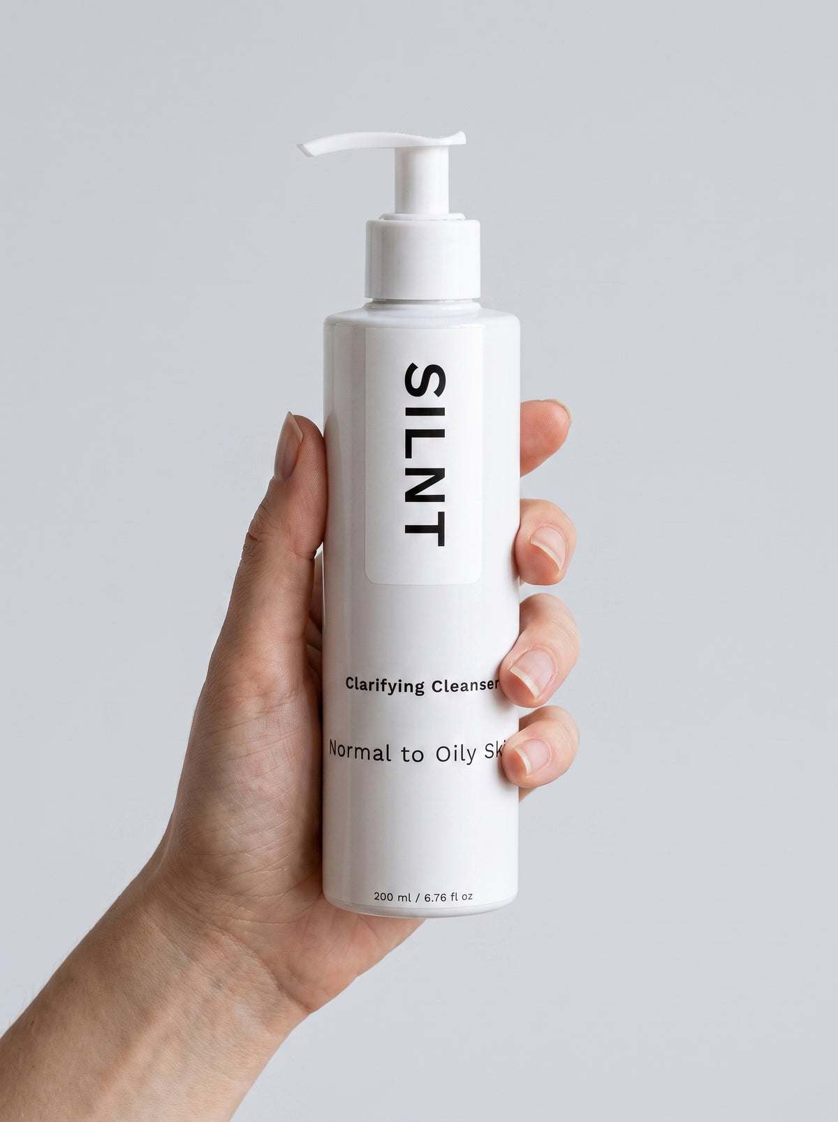 SILNT Clarifying Cleanser bottle held upright in one hand, showing its 200 ml size, light grey background