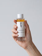 SILNT Makeup Remover bottle held upright in one hand, showing the two separated phases, light grey background