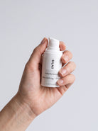 SILNT Daily Moisturizer travel size bottle held upright in one hand, showing its 15 ml size, light grey background