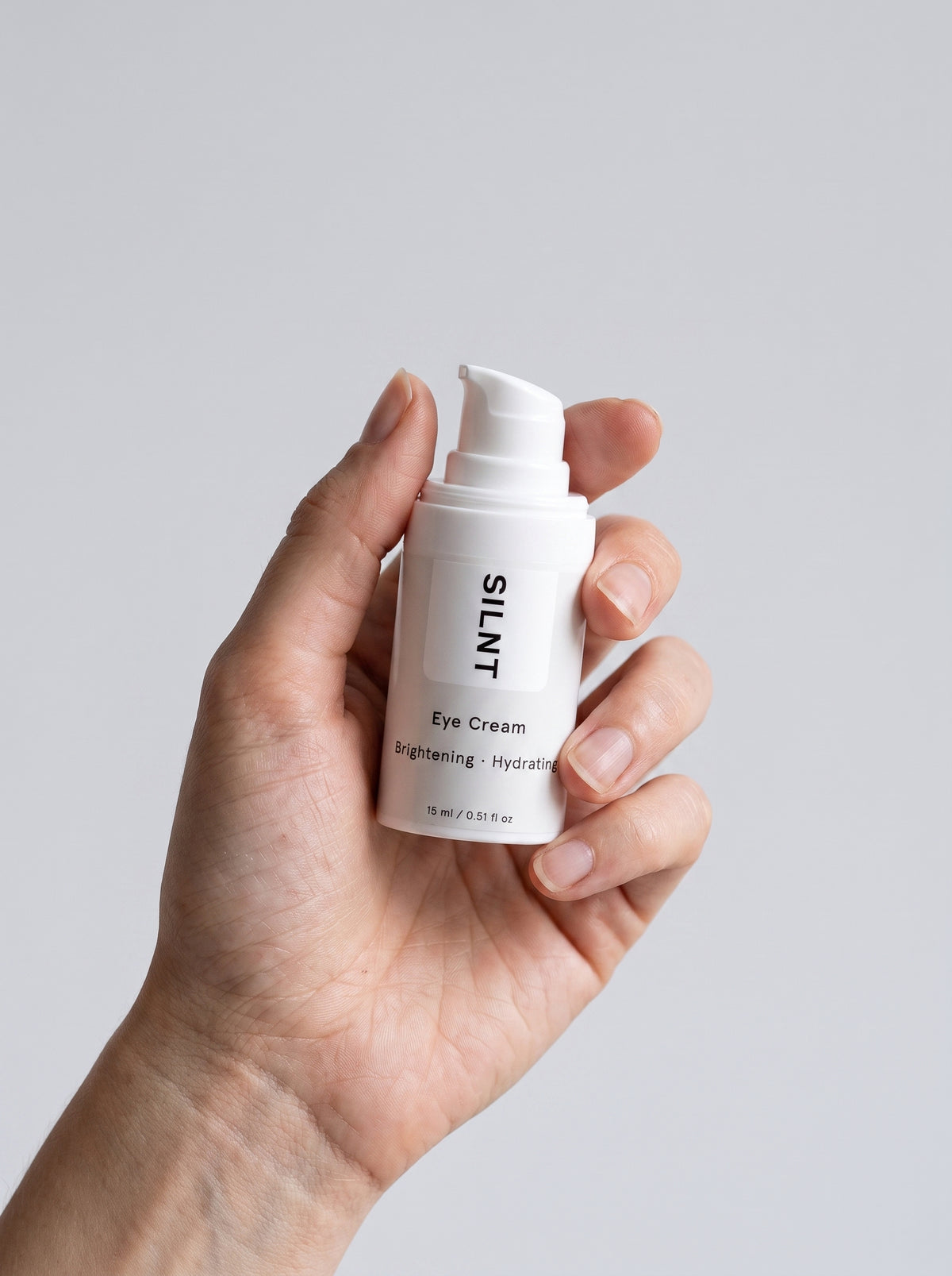 SILNT Eye Cream bottle held upright in one hand, showing its 15 ml size, light grey background
