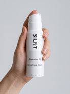 SILNT Cleansing Oil bottle held upright in one hand, showing its 150 ml size, light grey background