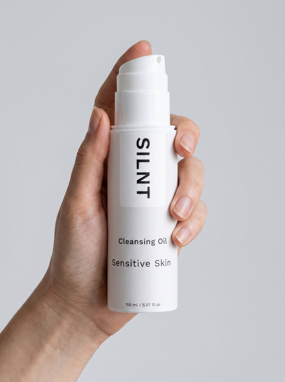 SILNT Cleansing Oil bottle held upright in one hand, showing its 150 ml size, light grey background