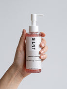 SILNT Radiance Cleanser bottle held upright in one hand, showing its 145 ml size, light grey background