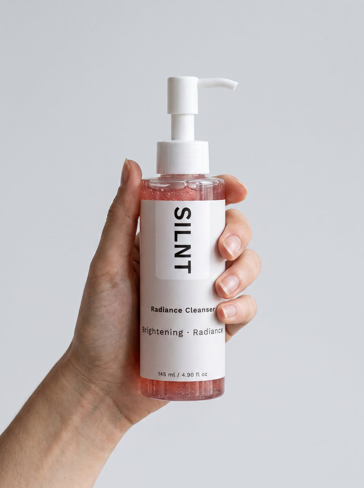 SILNT Radiance Cleanser bottle held upright in one hand, showing its 145 ml size, light grey background