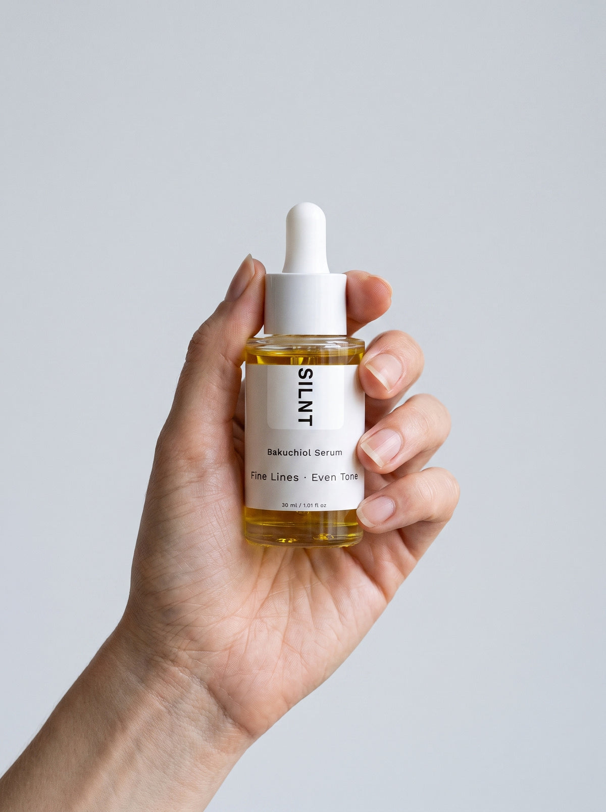 SILNT Bakuchiol Serum bottle held upright in one hand against a light grey background