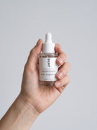 SILNT Exfoliating Concentrate bottle held upright in one hand against a light grey background
