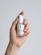SILNT Brightening Serum bottle held upright in one hand against a light grey background