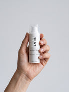 Hand holding the SILNT Vitamin C Serum bottle against a grey background