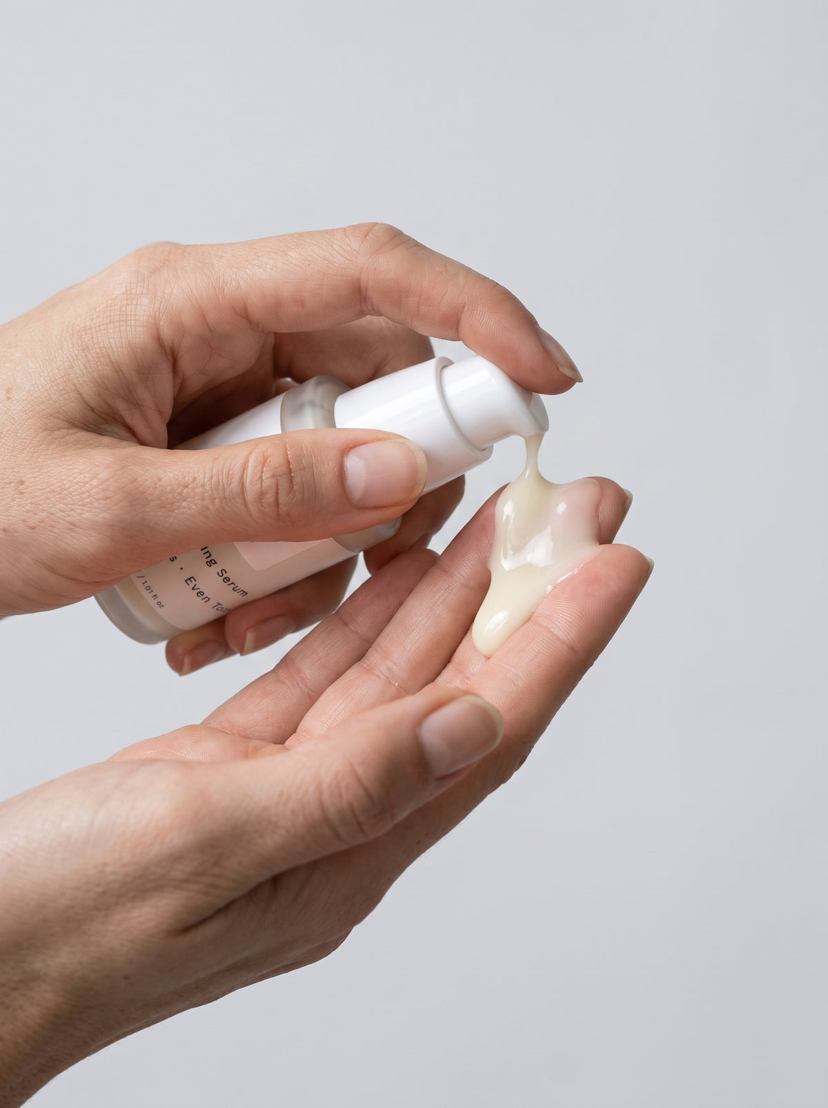 SILNT Brightening Serum bottle held in both hands with the pump facing forward, light grey background