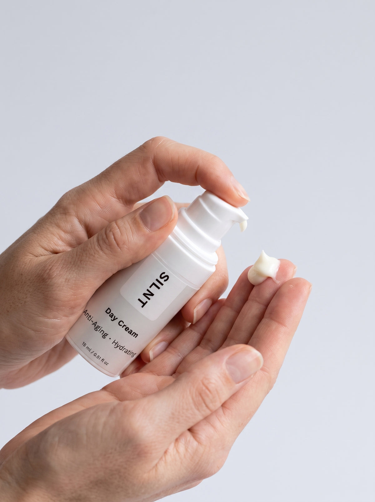 SILNT Day Cream travel size bottle held in both hands with the pump facing forward, light grey background
