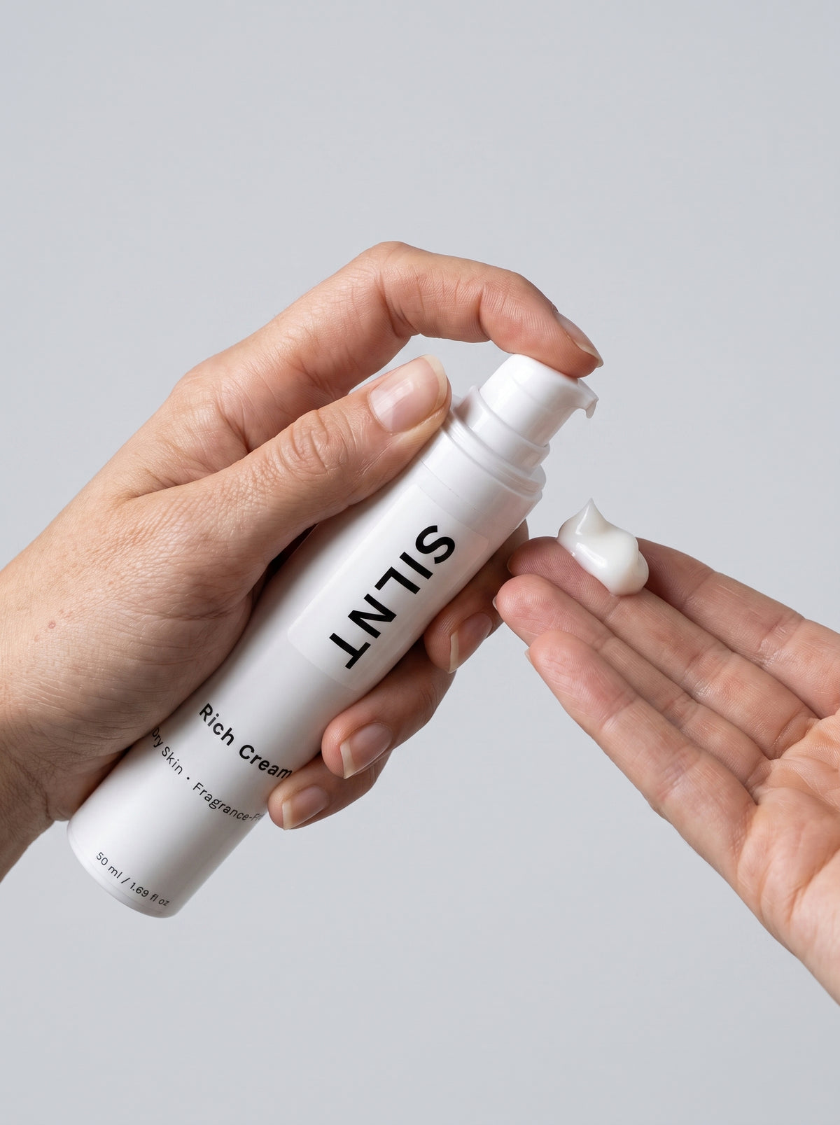 SILNT Rich Cream bottle dispensing thick white cream onto fingertips, light grey background