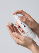 SILNT Clarifying Moisturiser bottle dispensing pale green cream onto fingertips, light grey background