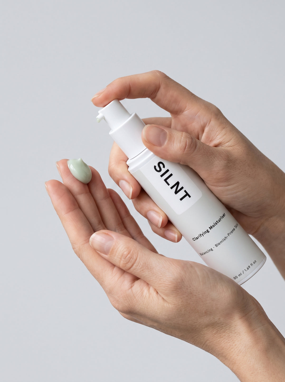 SILNT Clarifying Moisturiser bottle dispensing pale green cream onto fingertips, light grey background