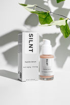 SILNT Peptide Serum bottle beside its carton with soft leaf shadows on a white surface