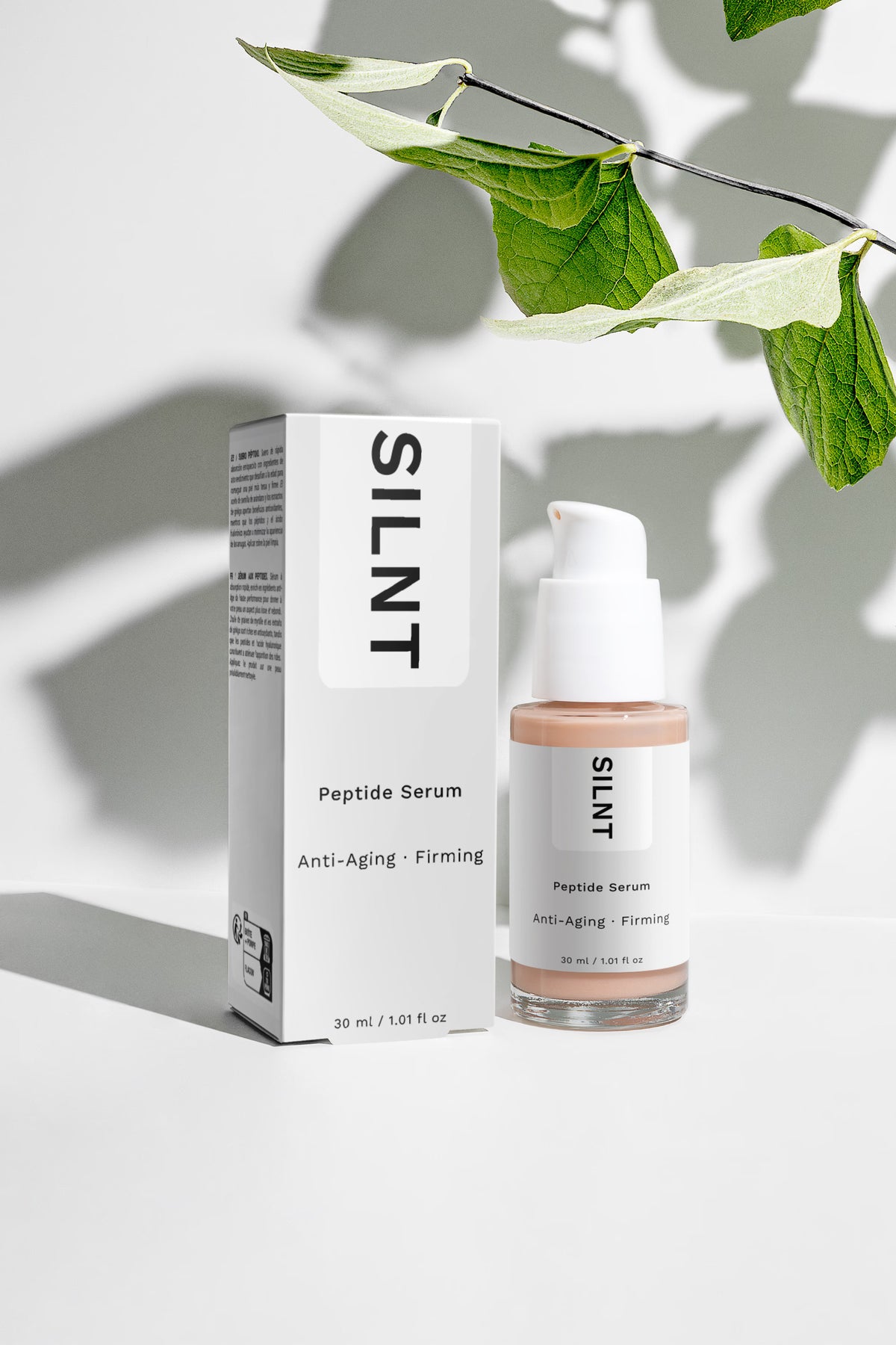 SILNT Peptide Serum bottle beside its carton with soft leaf shadows on a white surface