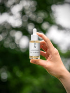 A hand holding SILNT Exfoliating Concentrate against green leaves