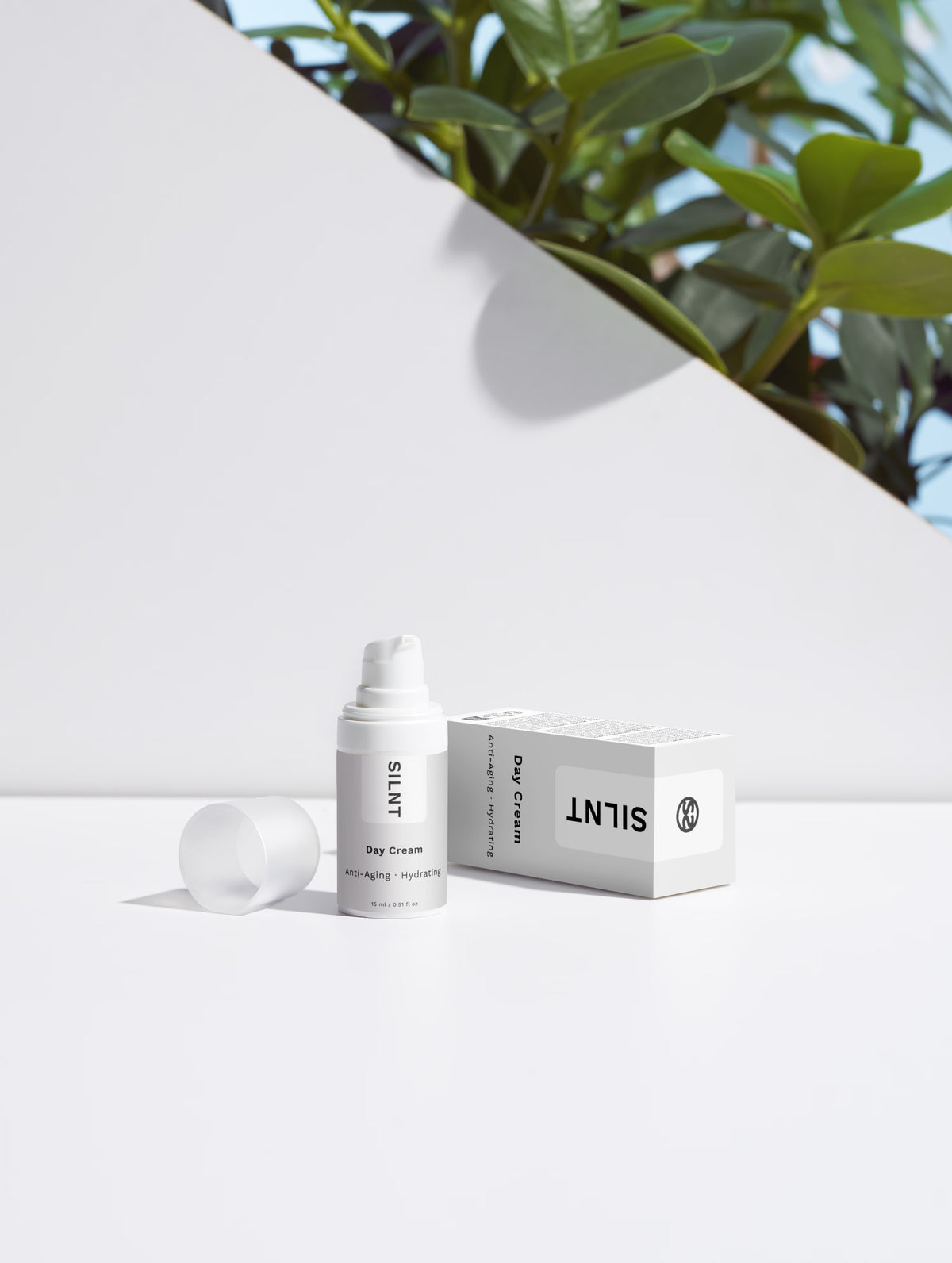 SILNT Day Cream travel size bottle beside its carton with soft leaf shadows on a light grey background