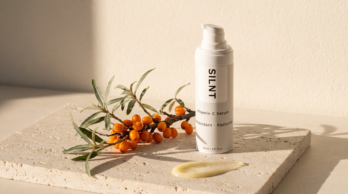 SILNT Vitamin C Serum on a travertine slab beside a branch of sea buckthorn in warm morning light
