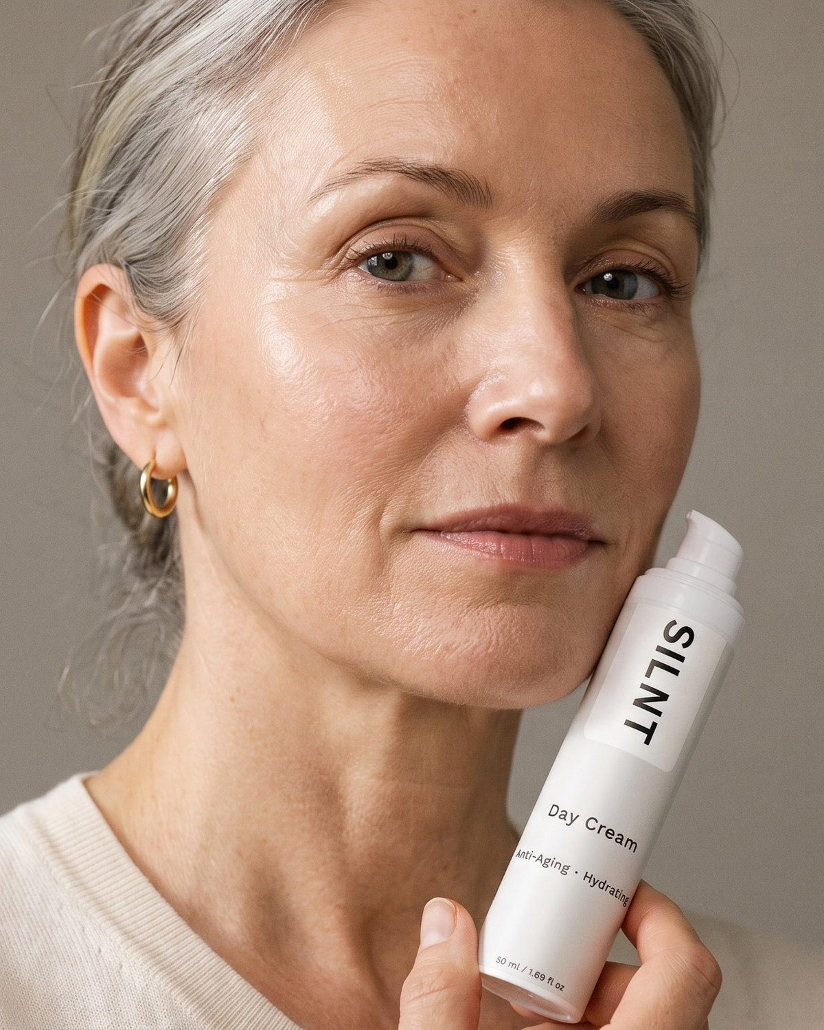 A woman with silver hair holding SILNT Day Cream against her jaw