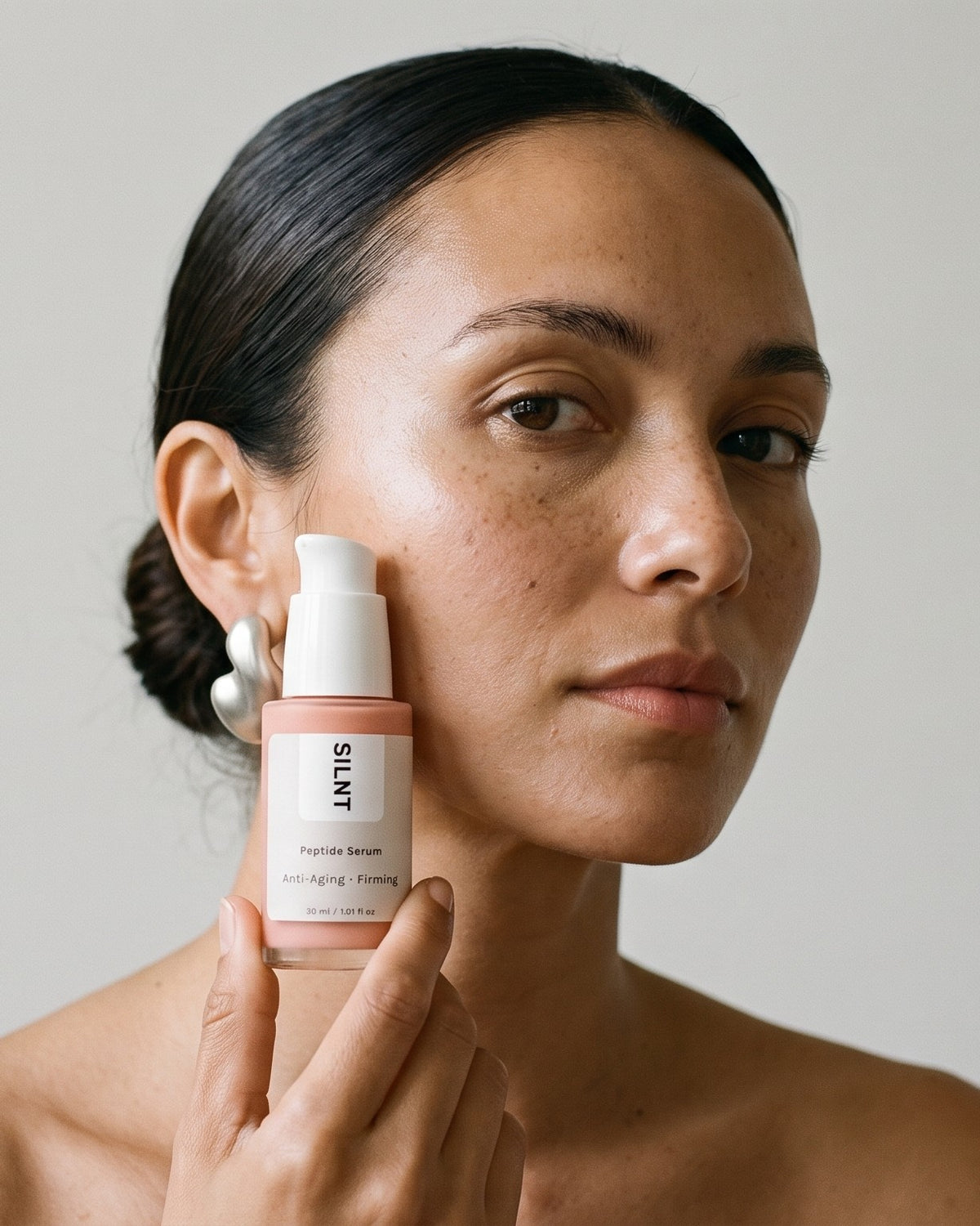 A woman holding SILNT Peptide Serum against her cheek
